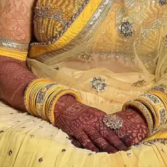 A stunning professional photo showing the final, dark henna stain on a bride. Paired with her yellow dress and bangles, the deep red of the mehndi looks absolutely perfect.