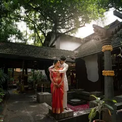 A full-body portrait of a couple in the courtyard of a traditional South Indian home. The heritage architecture provides a rich and culturally significant setting for their love story.