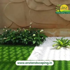 A clean and modern landscape design using high-quality artificial turf contrasted with a border of white pebbles and peace lily plants.