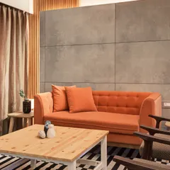 This living area showcases a powerful contrast between a warm, vibrant orange sofa and a cool, industrial-style concrete panel wall. The striped rug adds another layer of bold pattern, creating a space that is both edgy and inviting.