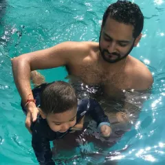 A father gently guides his son through the water, a perfect example of learning together.