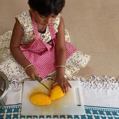 A child carefully practices her knife skills, slicing mangoes for our kitchen activity. Using child-safe tools, I guide them in developing practical life skills, confidence, and fine motor control in a supervised environment.