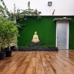 A tranquil patio space with a wooden deck, an artificial grass wall, and a Buddha statue as the focal point. This creates a perfect spot for meditation or quiet relaxation.