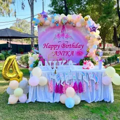 A beautiful outdoor unicorn party setup for Anika's 4th birthday. The main table features a rainbow and unicorn backdrop, a tassel garland, and a large gold foil '4' balloon.