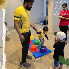 Here's a close-up of our bucket-walking exercise. A coach provides a steady hand while another child watches and claps, creating a supportive and encouraging atmosphere for learning new skills.
