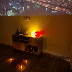 The living room is set up for a cinematic experience. A movie is projected onto the wall above a console table, with candles and rose petals on the floor to enhance the romantic mood.