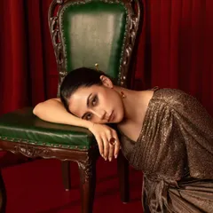 A quiet, emotive portrait for a brand campaign. The model's pose and the rich, warm tones of the lighting create a feeling of intimacy and luxury, highlighting the texture of the metallic dress.