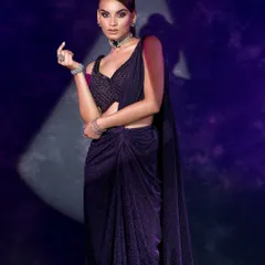 A full-body shot capturing a modern, pre-draped purple saree. The use of a spotlight creates a theatrical, moody atmosphere perfect for an editorial story.