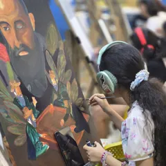 A young student, focused and in her own world with headphones on, carefully paints a portrait during class.