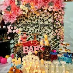 A cute and cozy setup for a baby's birthday or naming ceremony. The decor includes a sequin backdrop, a floral and tulle arch, and light-up marquee letters spelling the baby's name.