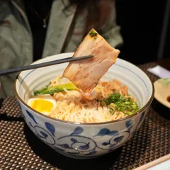 A piece of tender pork belly from our Ebisu Ramen, held up by chopsticks. The pork is slow-cooked until it is perfectly tender and flavorful.