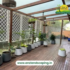This sunroom project at Good Earth Malhar features a wooden frame, a translucent roof, and white lattice panels for privacy. The space is filled with exotic plants in modern pots, creating a beautiful indoor garden.