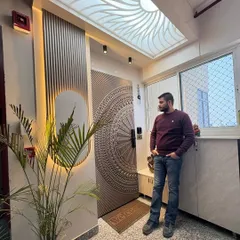 Standing next to a completed grand entrance at Nirala Estate. The design features an intricately carved main door, a backlit CNC-cut ceiling panel, and a fluted wall panel with accent lighting.