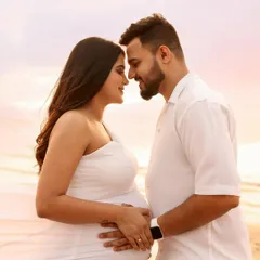 An intimate close-up against a sunset sky. The warm, golden light of the setting sun creates a romantic and dreamy atmosphere for this beach maternity portrait.
