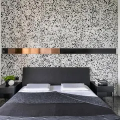 The guest room in 'A Wedged Haus' features a neutral palette of terrazzo and grey stone. The design is punctuated by a copper cuboid wedged into the headboard, creating a sharp, metallic focal point.