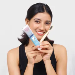 A clean and friendly lifestyle shot for an oral care brand. The model holds the toothpaste and toothbrush, looking directly at the camera to build a connection and trust with the viewer.
