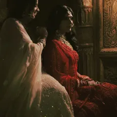 Lost in thought, a bride shares a final moment of calm with her loved one before the festivities. The warm, soft lighting and rich wooden background create an intimate, painterly portrait.