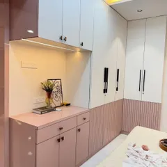 A beautiful example of a two-tone wardrobe in dusty pink and white. The design includes fluted paneling and a built-in desk area with overhead cabinets, making it a multi-functional piece of furniture perfect for a modern bedroom.