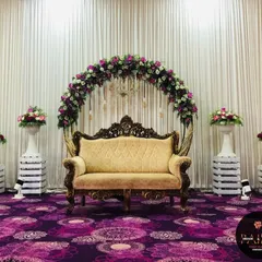 I designed this elegant stage for a ring ceremony, featuring a classic floral arch in purple and white. The ornate golden sofa provides regal seating for the couple, creating a perfect photo opportunity for their special day.