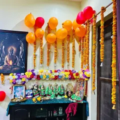 Another view of the decorated pooja space, highlighting the fresh marigold strings hanging next to the door and the arrangement of deities on the cabinet.