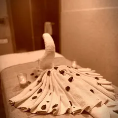 A close-up of the thoughtful details that await you. A towel folded into an elegant peacock design, scattered with petals, shows the care we put into making every moment of your visit special.