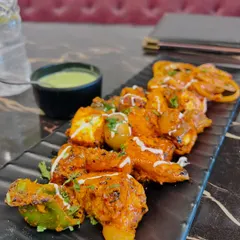 A classic paneer tikka appetizer. This shot is framed to show the texture of the grilled paneer and vegetables, served with a side of mint chutney, a staple of North Indian cuisine.