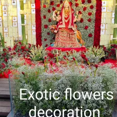 A magnificent floral stage for a Navratri celebration, featuring a large Devi idol. The backdrop is a dense wall of red roses, framed by white floral pillars and a sea of baby's breath, creating a powerful and devotional setting.