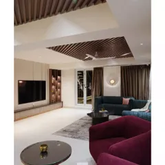 A full view of the living room, showcasing the interplay of textures and forms. The deep maroon armchairs add a pop of color against the neutral travertine wall, while the slatted wood ceiling adds warmth and architectural interest.