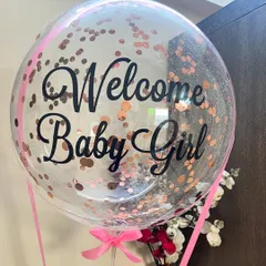 A close-up of our custom 'Welcome Baby Girl' balloon, filled with sparkling rose gold confetti and tied with a pretty pink ribbon. Every detail is designed to be picture perfect.