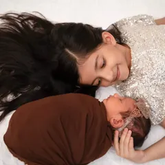 An older sister lies next to her newborn sibling, sharing a quiet, loving gaze. This image captures the beautiful, unfolding story of sibling love, a precious interaction that we believe is essential to include in your family's first portraits together.