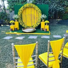 An outdoor Haldi setup with a beautiful circular backdrop made of yellow flowers and hanging tassels. We arranged the seating and traditional brass 'urli' for the ceremony, ensuring every detail was perfect.
