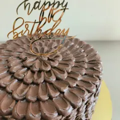 A close-up of the intricate chocolate petal piping and the elegant gold "Happy Birthday" topper.