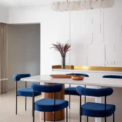 We love adding a pop of color to create drama and personality. In our 'Vishu Home' project, these bold, royal blue velvet chairs stand out against the monolithic white dining table and textured wall, creating a modern yet timeless dining experience that is both elegant and inviting.