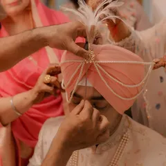 A close-up of the Sehra Bandi ritual, where the groom's turban is lovingly adorned by his family members before the ceremony begins.
