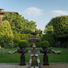 We create classic, formal gardens that evoke timeless elegance. This space is defined by its perfect symmetry, featuring a central tiered water fountain, meticulously manicured topiary, and lush green lawns bordered by high privacy hedges.
