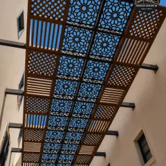 A view looking up at a custom CNC-cut pergola roof. The geometric pattern allows sunlight to filter through, creating a dynamic and visually interesting experience that changes throughout the day.