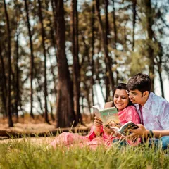 A sweet moment of the couple reading a book together, nestled in the grass in a beautiful woodland setting.