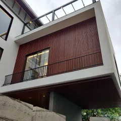 The "after" shot of a residential facade, featuring a finished wood-paneled exterior and glass-railed balcony.
