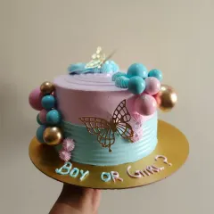 A "Boy or Girl?" gender reveal cake in pastel pink and blue, decorated with golden butterflies and decorative spheres.