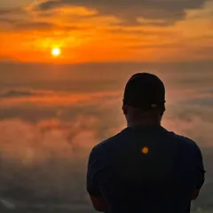 A trekker watching the sky turn orange as the sun rises above a sea of clouds at Uttari Betta.