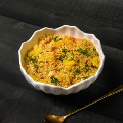 A simple and nutritious quinoa salad with yellow peppers and fresh parsley, presented in a white bowl on a dark table.