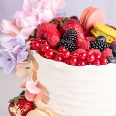 A close-up of the top tier, showing the beautiful arrangement of summer berries, macarons, and edible gold leaf.