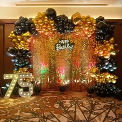 An elegant 75th birthday celebration with a gold sequin backdrop. The decor is accented with black and gold balloons and large marquee numbers, creating a luxurious feel.