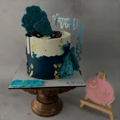 This abstract design uses shades of deep blue and white buttercream, accented with gold leaf and topped with dark blue chocolate sails.