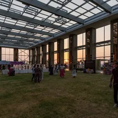 As dusk settles, the pavilion transforms into a glowing beacon. The structure's transparency creates a beautiful effect, with the interior activities visible from the outside and the sunset providing a stunning natural backdrop.