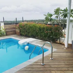 This view highlights the details of a residential terrace pool deck we designed in Mysore. The rich wooden decking is complemented by a privacy hedge of red-tipped photinia, adding color and seclusion to this private oasis.