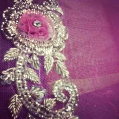 An extreme close-up of 3D zardozi embroidery on a purple net fabric. This technique uses metallic threads and embellishments to create a raised, textured floral design that is rich and luxurious.