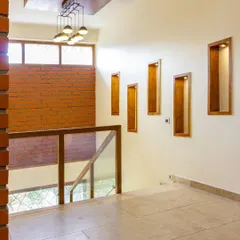 An exposed brick wall serves as a textured backdrop for the upper floor landing. The wooden niches are designed for displaying art, adding a personal touch to the space.