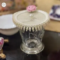 A close-up of a single embellished glass cover on an ornate glass. This piece features a delicate pink rose and a pearl-draped edge, perfect for protecting a drink at a garden party or bridal shower.