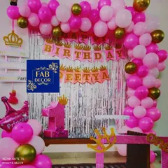 This princess-themed first birthday party features a pink and gold balloon arch, a silver shimmer curtain, and custom cutouts like the large number '1' and crowns. I also included a personalized name banner for the birthday girl, Deetya.